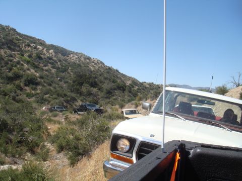 1992 Ford Bronco - Multiple SUVs and trucks are parked on a dirt road in a dry, hilly area under a clear blue sky.