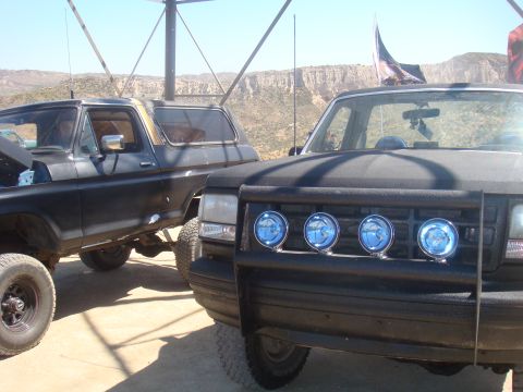 1992 Ford Bronco - Two modified SUVs are parked in a dry, hilly landscape under a bright sky.