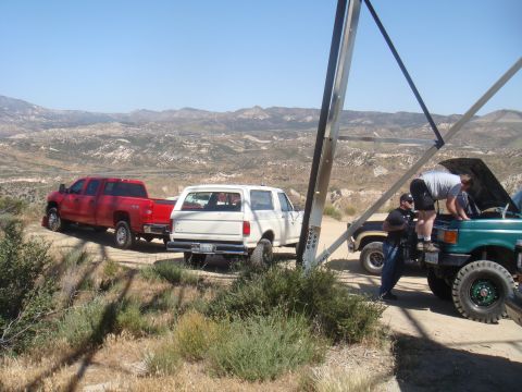 1992 Ford Bronco - A white 1992 Ford Bronco is parked on a dirt road, with other vehicles and people nearby, set against a mountainous landscape.
