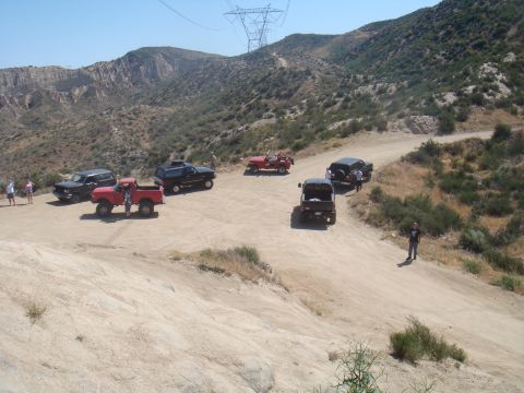 1992 Ford Bronco - A group of off-road vehicles navigates a dusty trail in a mountainous, arid landscape.