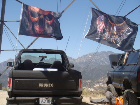 1992 Ford Bronco - A black Ford Bronco is parked outdoors with two flags flying overhead, and another vehicle is partially visible to the right.
