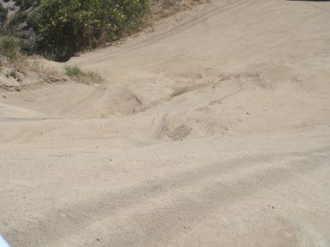1992 Ford Bronco - Tire tracks mark a path on a sandy dirt road with dry grass and bushes.