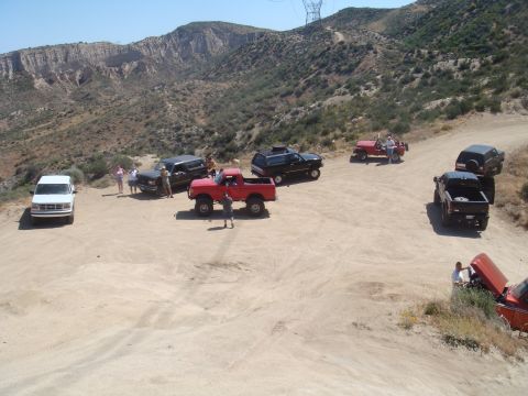 1992 Ford Bronco - Several off-road vehicles are gathered on a dusty trail with hills and power lines in the background.