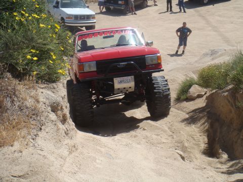 1992 Ford Bronco - Modified red Ford Bronco navigates a challenging off-road trail with another Ford truck in the background.