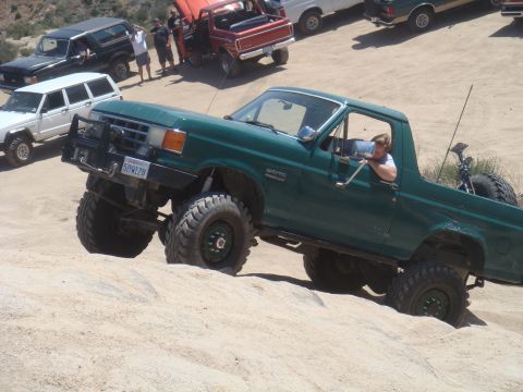 1992 Ford Bronco - A green Ford Bronco is shown off-roading with other vehicles in the background.