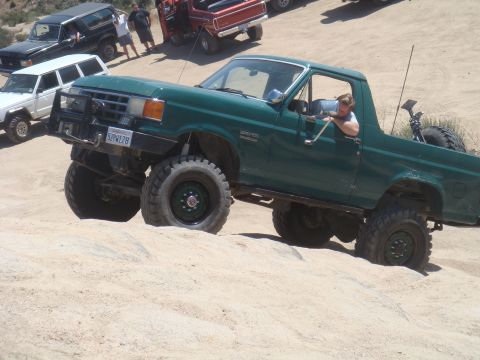 1992 Ford Bronco - This modified 1992 Ford Bronco navigates a sandy incline, with other off-road vehicles visible in the background.