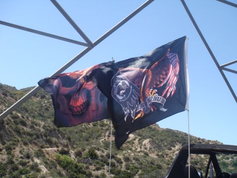 1992 Ford Bronco - Flags with skull and eagle designs fly from a vehicle against a backdrop of hills and sky.