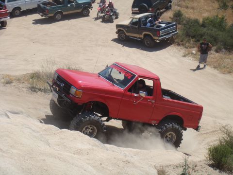 1992 Ford Bronco - A red pickup truck navigates a dirt trail with other vehicles present.