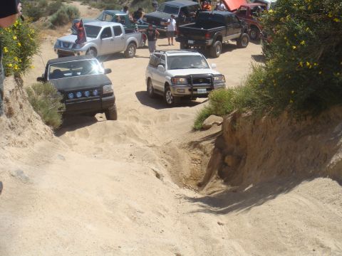1992 Ford Bronco - Multiple off-road vehicles are seen on a challenging sandy trail, with some vehicles climbing and others descending.