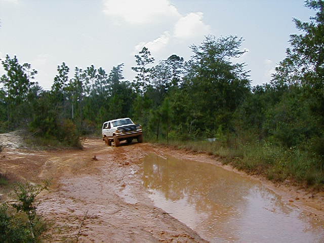 White 1990 Ford Bronco navigating a muddy trail with a large puddle