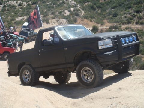 1992 Ford Bronco - Off-road Bronco navigating a dusty trail with other vehicles in the background.