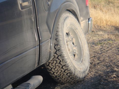 1992 Ford Bronco - The rear tire and side panel of a black truck are visible on a dirt road.