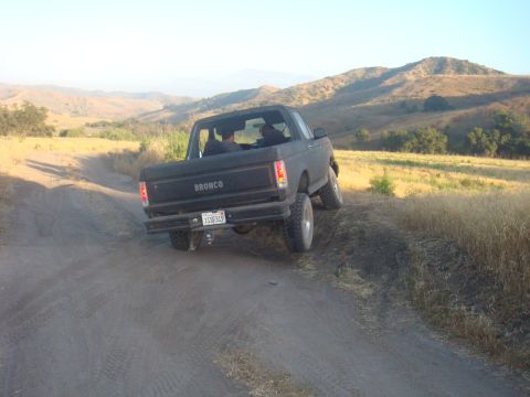 1992 Ford Bronco - A black Ford Bronco navigates a dusty trail through a dry, grassy landscape with rolling hills in the background.