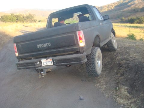 1992 Ford Bronco - Black Ford Bronco with 'BRONCO' on tailgate driving on a dirt road.