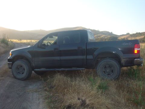 1992 Ford Bronco - A black pickup truck is parked on a dirt road with dry grass and hills in the background.