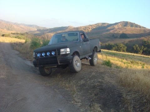 1992 Ford Bronco - This 1992 Ford Bronco navigates a dusty, off-road trail with hills in the background.