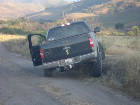 1992 Ford Bronco - This black Ford F-150 pickup truck is seen on a dirt road with its driver's side door ajar and a lifted suspension.