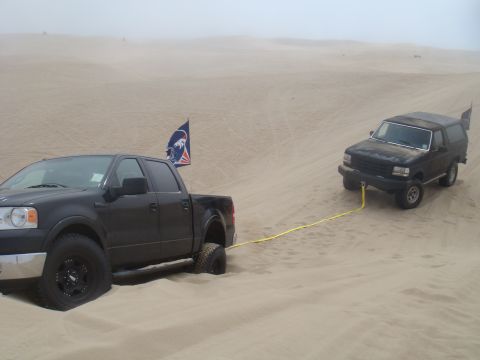 1992 Ford Bronco - A black 1992 Ford Bronco is being towed by a black pickup truck through sandy terrain.