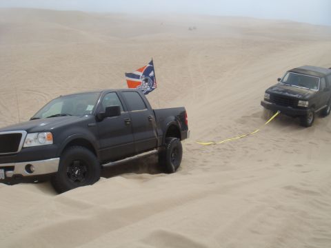 1992 Ford Bronco - Ford F-150 pulls a Ford Bronco out of the sand dunes with a yellow tow strap.