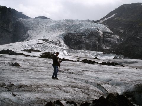 1996 Ford Bronco - A person stands on a vast icy landscape with a massive glacier in the background under a cloudy sky.