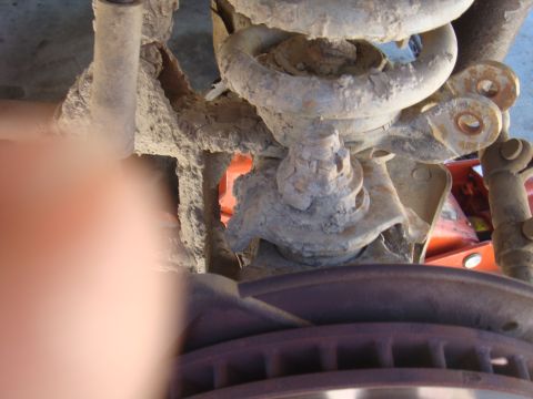 1992 Ford Bronco - This image shows the heavily corroded suspension system of a vehicle, with a brake rotor and an orange jack visible.