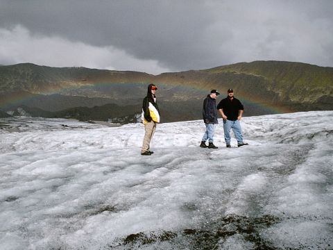 1996 Ford Bronco - A rainbow arcs over a mountainous landscape as three individuals stand on a glacier.