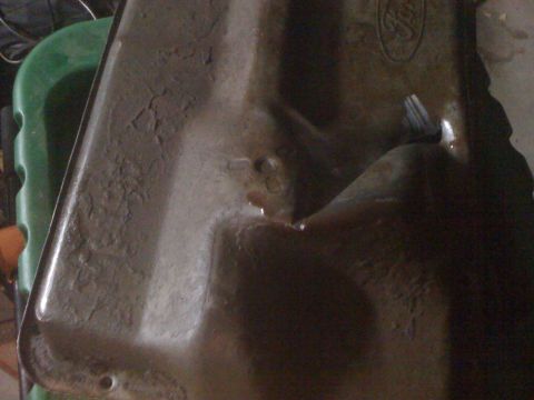 1992 Ford Bronco - A close-up view of a worn oil pan, showing signs of damage and fluid leakage.