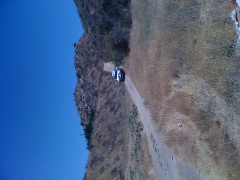 1992 Ford Bronco - A white 1992 Ford Bronco navigates a dusty mountain road under a clear blue sky.