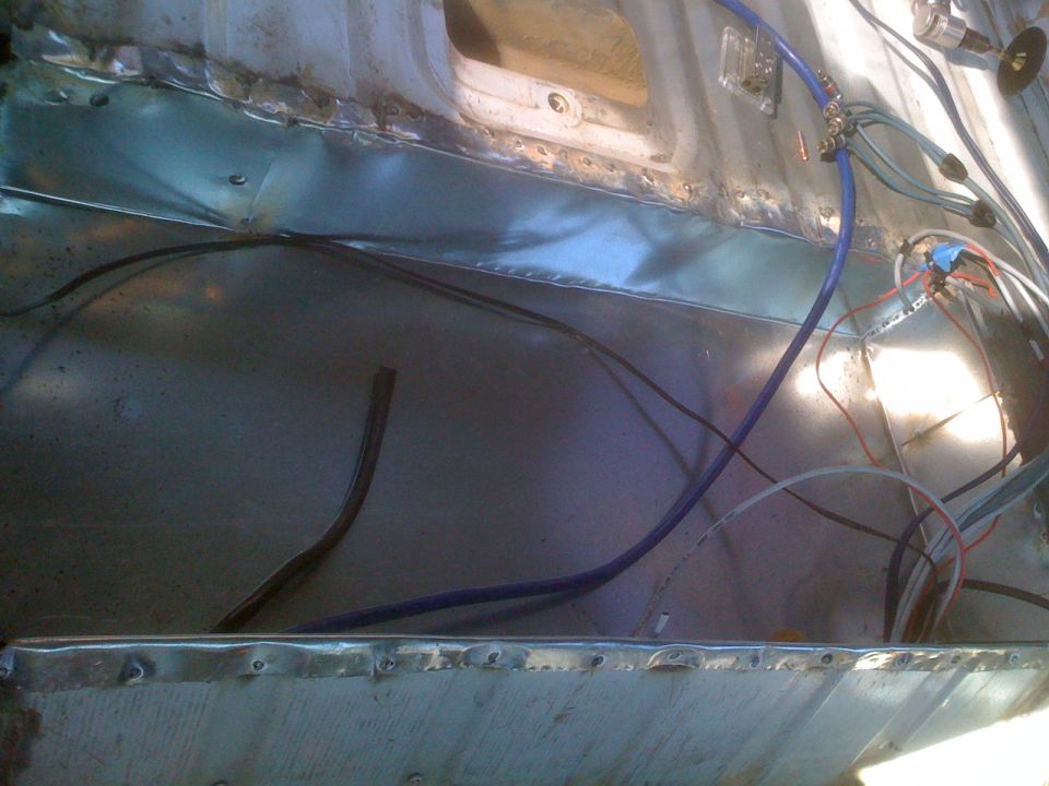 Interior of a vehicle showing exposed metal floor and wiring, with visible welds and rivets