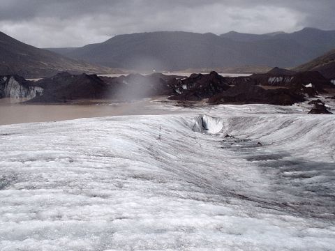 1996 Ford Bronco - Glacier landscape with ice formations, muddy water, and distant mountains under an overcast sky.