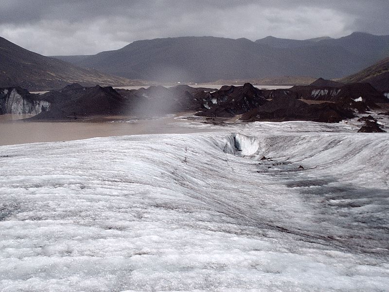 Glacier ice field with dark moraine ridges and stormy mountains behind