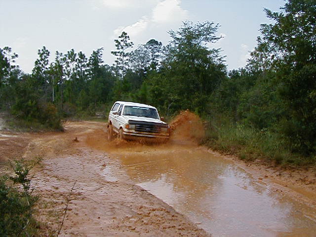 White 1990 Ford Bronco splashes through mud puddle