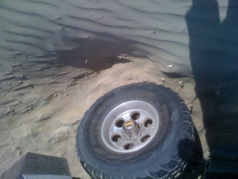 1992 Ford Bronco - Vehicle tire in sand dunes, with a shadow of a person visible.