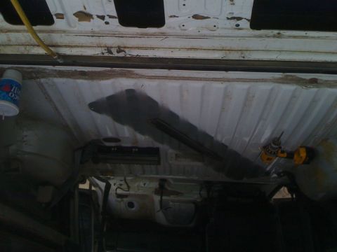 1992 Ford Bronco - The underside of a vehicle is being worked on with a drill, showing exposed metal and some rust.