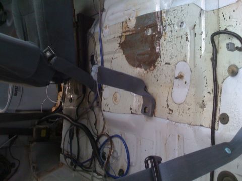 1992 Ford Bronco - The interior of a vehicle shows exposed metal panels, wiring, and seatbelt anchors, suggesting a stripped-down or modified state.