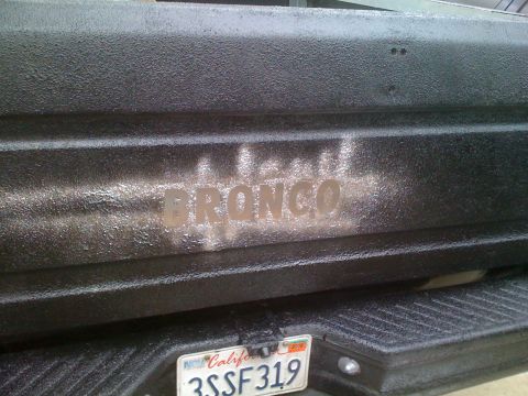 1992 Ford Bronco - The word "BRONCO" is visible on the textured tailgate of a vehicle, with a California license plate below.