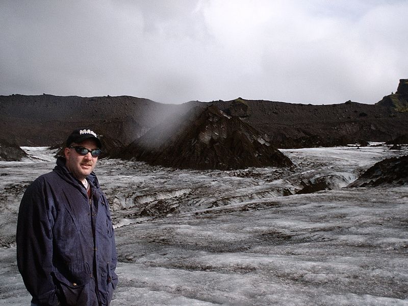 Man in blue jacket and cap standing on a glacier under cloudy sky