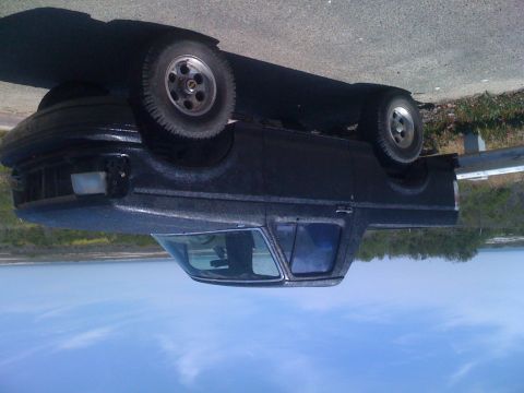 1992 Ford Bronco - A dark-colored pickup truck is parked on a paved surface next to a body of water.