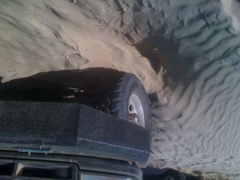 1992 Ford Bronco - A vehicle navigates sandy terrain, with its spare tire prominently visible against the dune landscape.