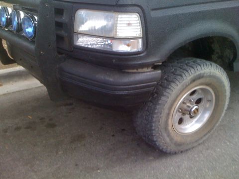 1992 Ford Bronco - Close-up of a truck's front wheel, bumper, and headlight assembly.