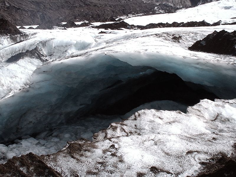 Blue ice cave in a glacier surrounded by snow and rock