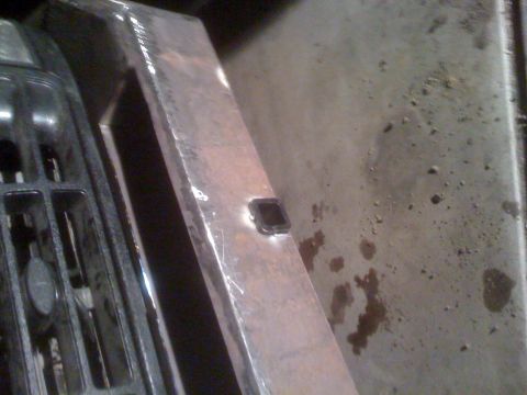 1992 Ford Bronco - A close-up view of a metal bracket with a square hole, likely a component of a vehicle's front end assembly.