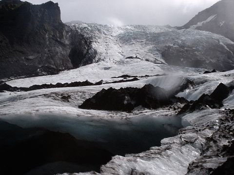 1996 Ford Bronco - A vast glacier stretches across a mountainous landscape, with dark rocks emerging from the ice and a dark pool of water in the foreground.