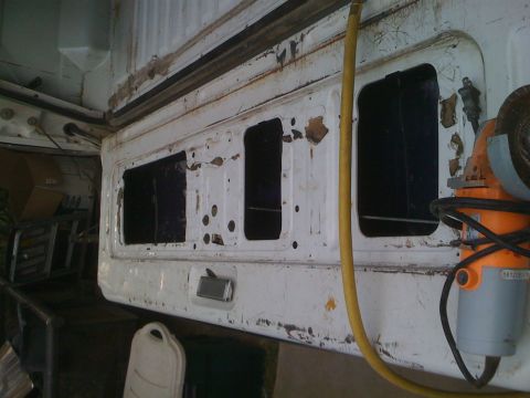 1992 Ford Bronco - A white tailgate with multiple cutouts is shown, with a yellow hose and a grinder nearby.