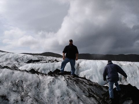 1996 Ford Bronco - Two individuals navigate a rocky, icy landscape with a dramatic cloudy sky overhead.