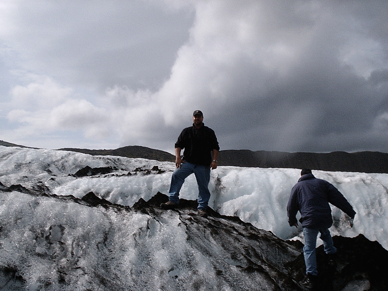 Two men standing on a glacier under a cloudy sky