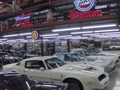 1979 Chevrolet Camaro - Several white Pontiac Trans Am cars are parked in a showroom with various signs and memorabilia on the walls.