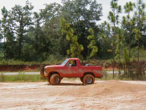 1990 Ford Bronco - A red pickup truck navigates a dirt track with trees in the background.
