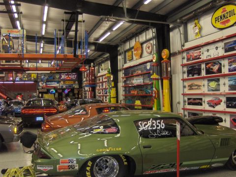 1979 Chevrolet Camaro - A green 1979 Chevrolet Camaro drag car is parked in a garage filled with memorabilia and other vehicles.