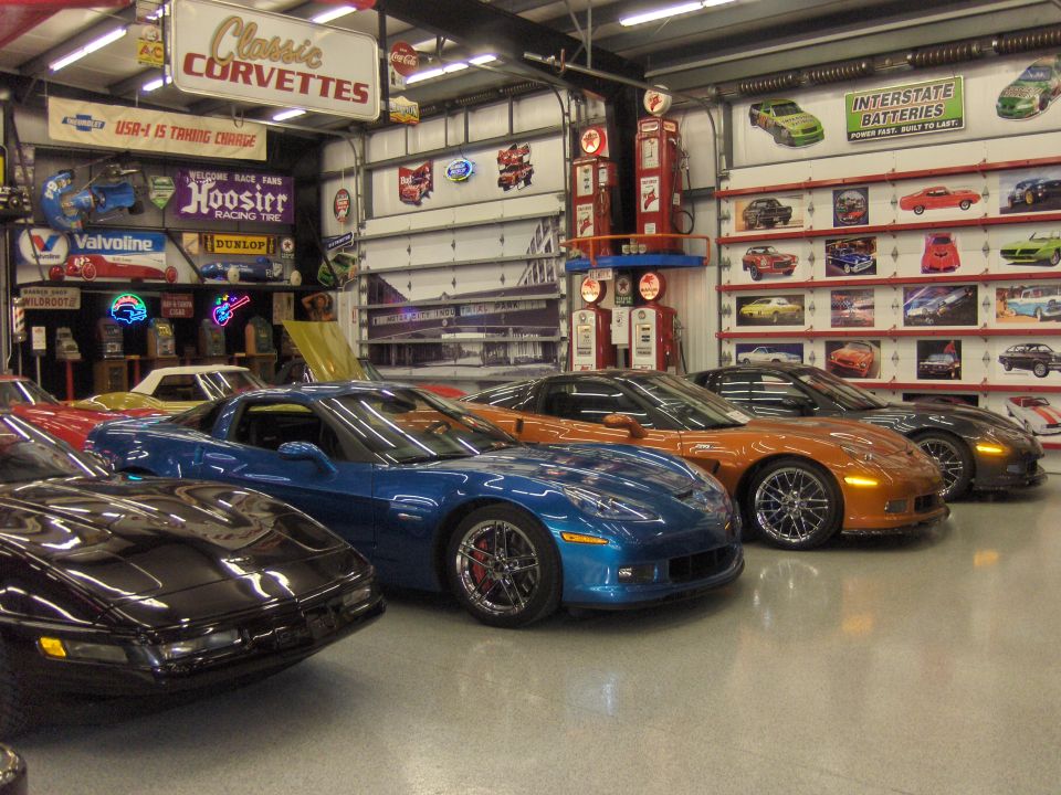 Several Corvettes parked in a garage with vintage signs and gas pumps